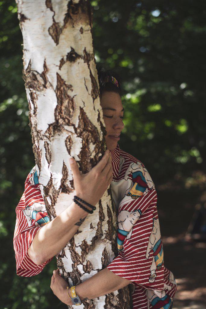 Mixed race non-binary person hugging birch tree in forrest