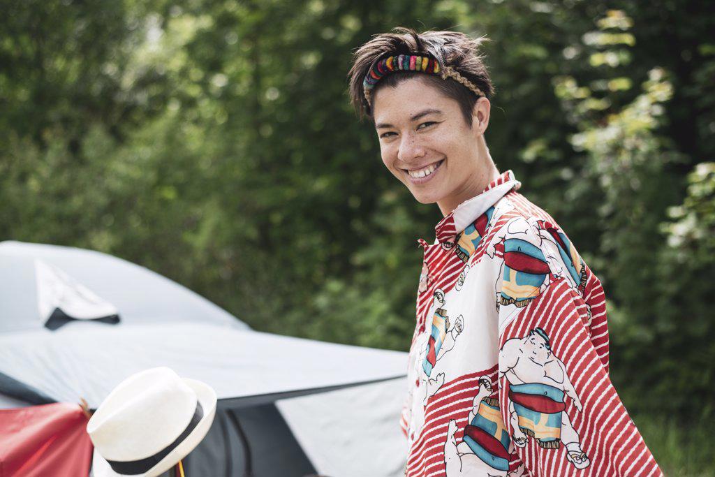 Smiling queer mixed-race woman colourful shirt, headpiece in campsite
