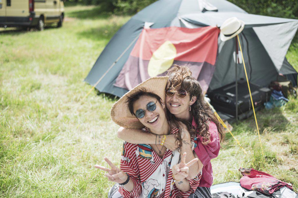 Smiling queer couple in colourful clothes camping at festival