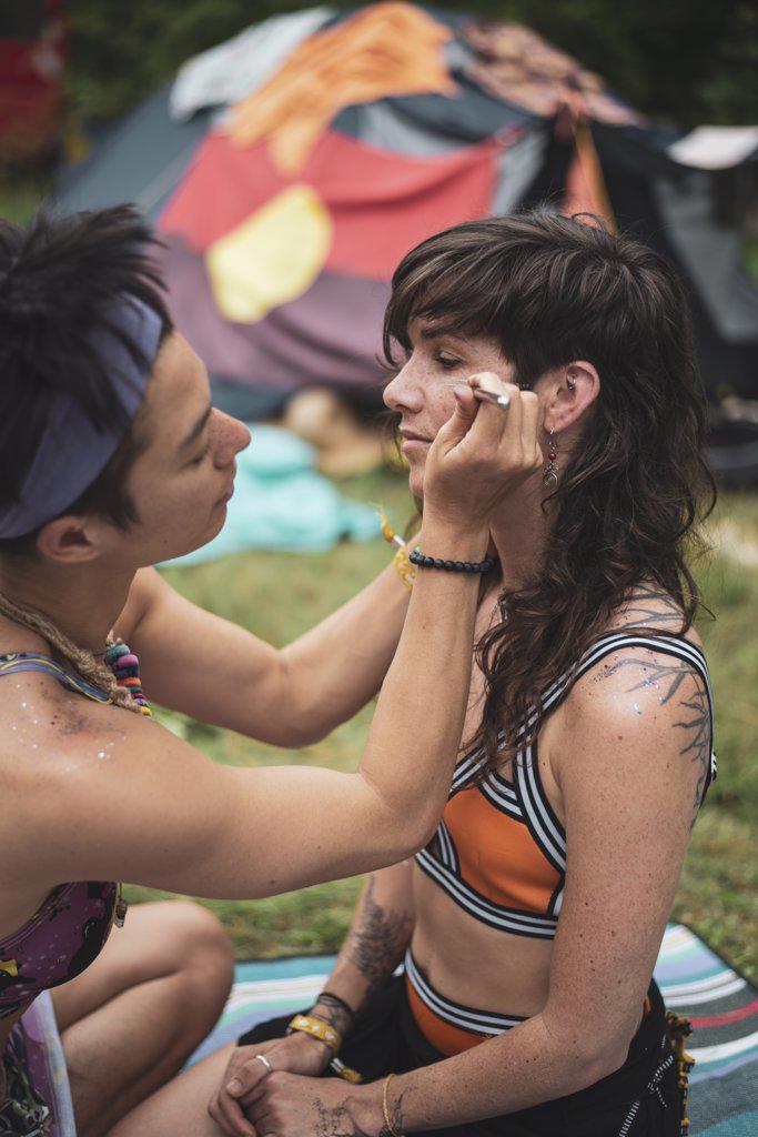 two fit healthy queer women paint face and glitter body at camp