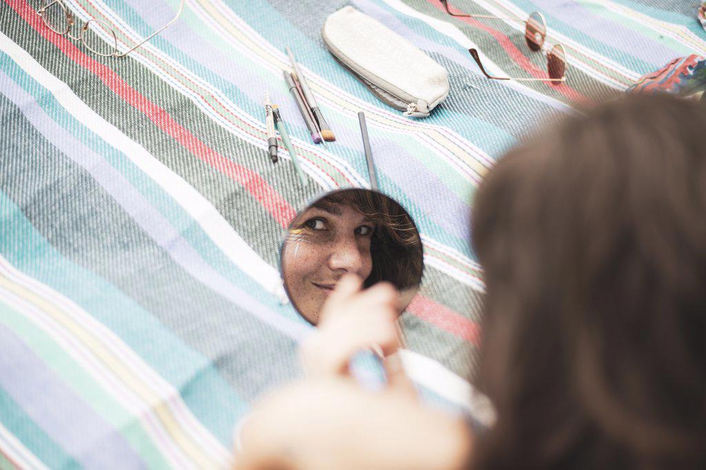 Artistic woman's reflection in mirror facepainting on summer blanket