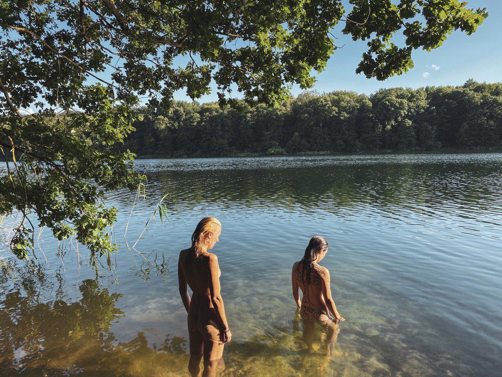 two beautiful natural women stand nude in green lake in europe