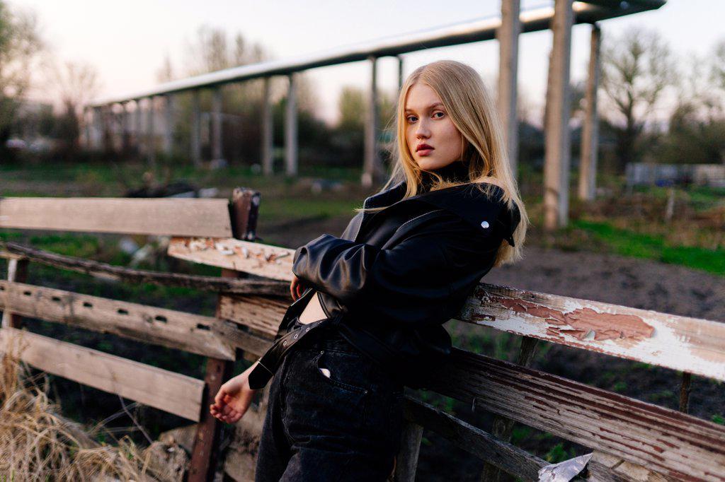 Stylish blonde woman standing near a wooden fence in a leather jacket
