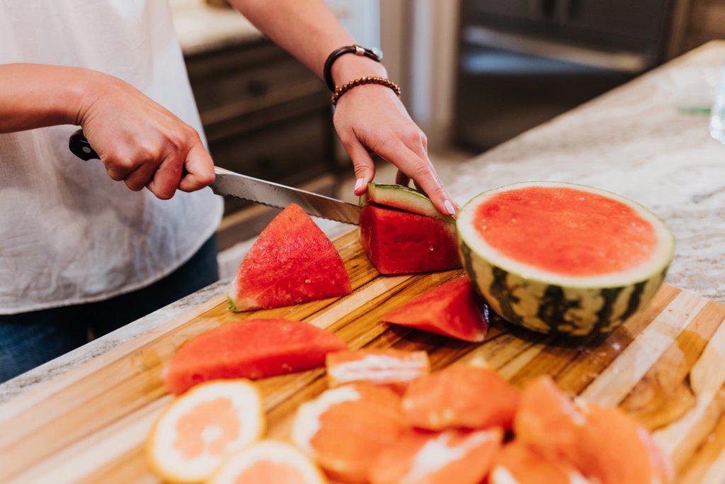Close up of woman slicing watermelon and other fruits in her kitchen