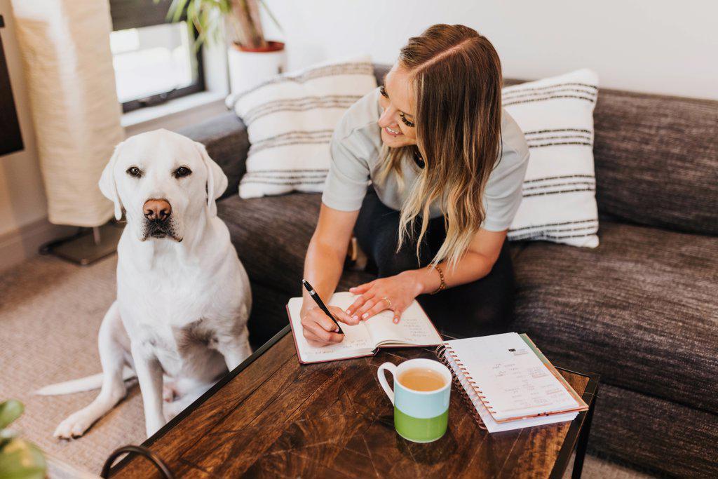 Woman writes in notebook while looking at her dog