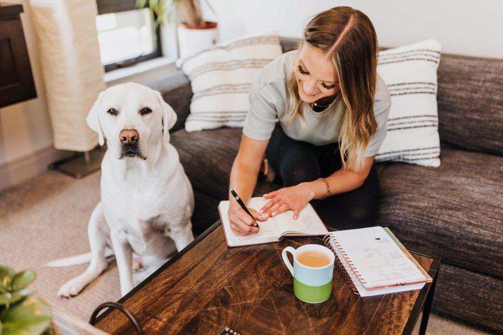 Woman writes in notebook while dog sits next to her