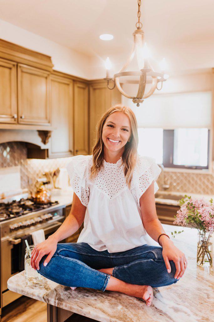 Smiling woman sitting on kitchen counter looks at camera