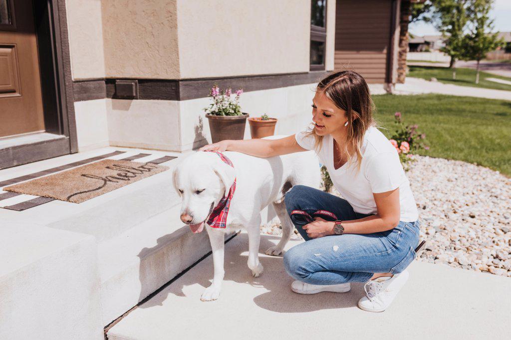 Woman kneels on her front step while petting her dog