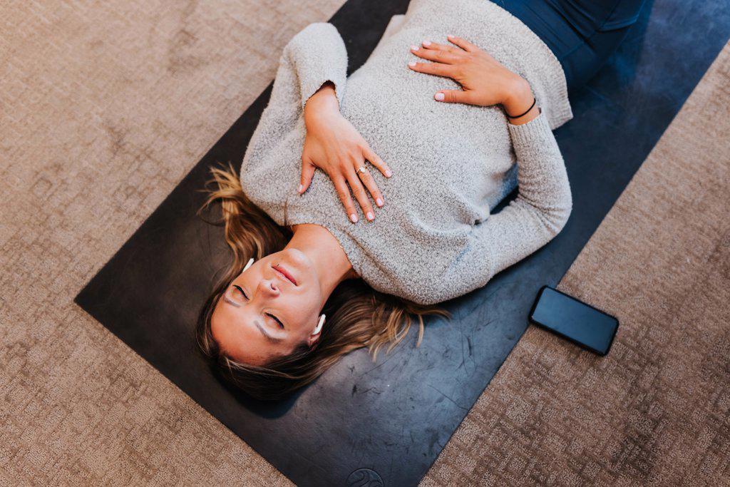 Woman meditates while laying on yoga mat in her home