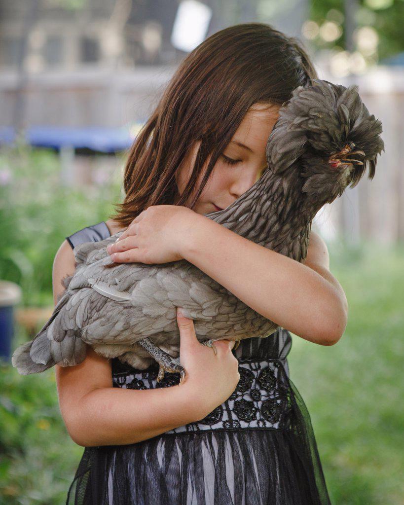 Beautiful girl, eyes closed, tenderly holds a pet chicken in her arms