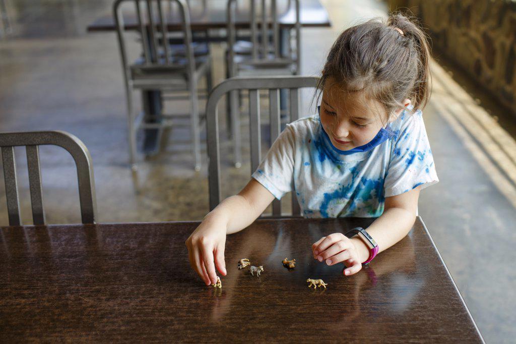 A little girl sits at a table playing with tiny toy animals