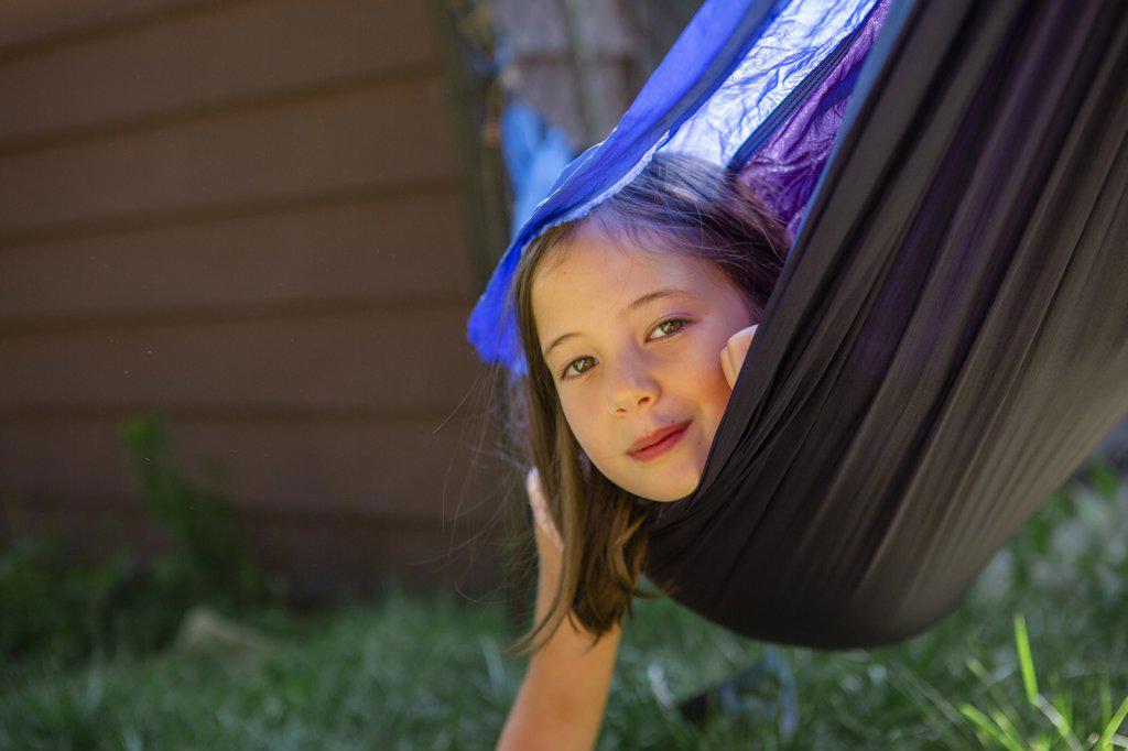 A cute little girl with direct gaze plays in a hammock outside