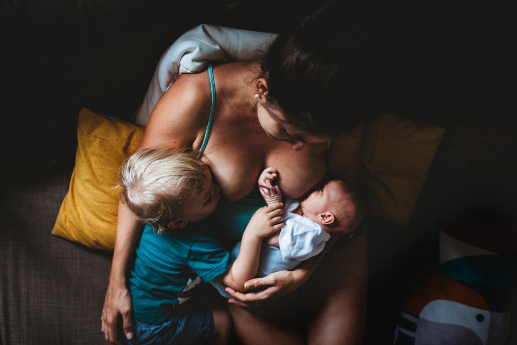 Mom tandem breastfeeding newborn baby and toddler