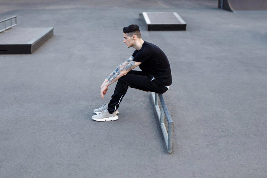 young brunette man sitting alone on an asphalt skate playground