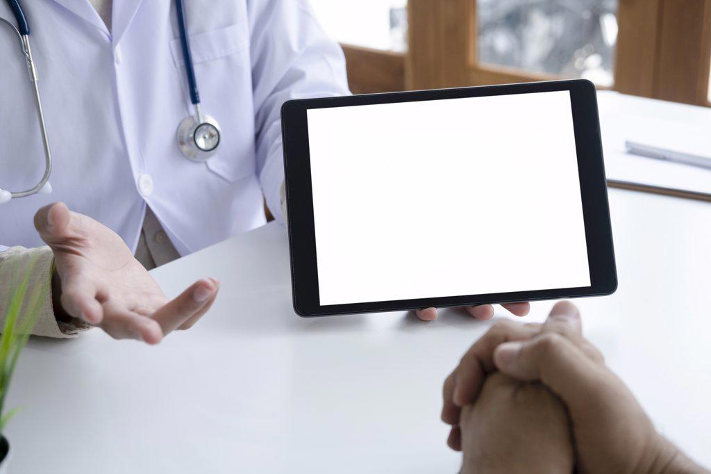 Doctor using computer tablet discussion something with patient.