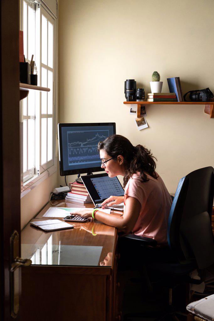 Female broker trading on stock market using laptop from home office.