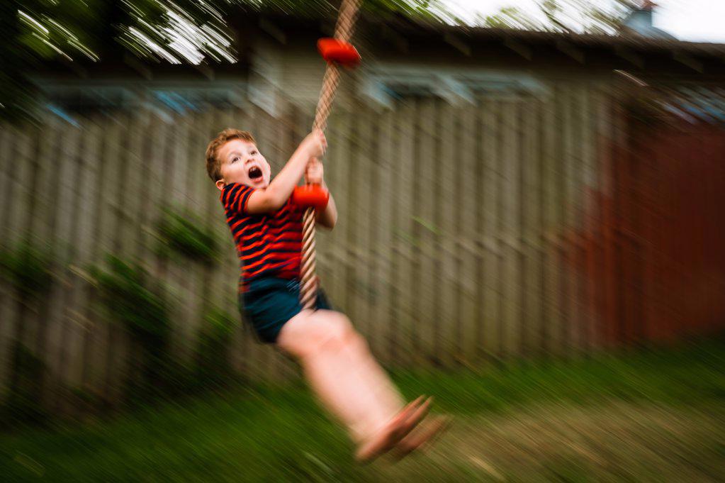Young boy shouting with joy on rope swing in motion.
