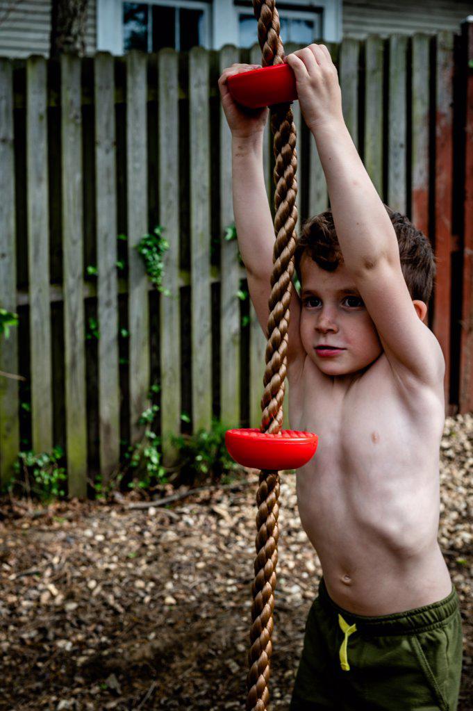 Little boy with dirty face and dreamy expression hanging on rope swing