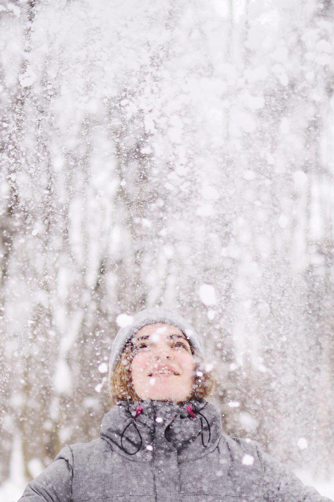 A young woman looks with delight at the falling snow in the forest.