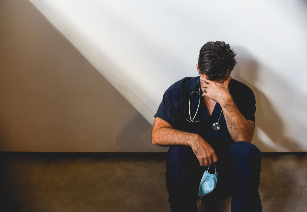 Exhausted doctor wearing scrubs sitting on floor in a patch of light.