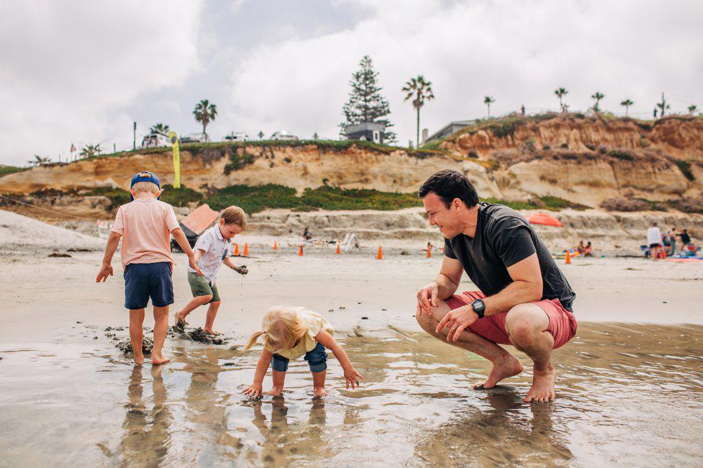 Dad plays happily with kids on Moonlight beach in San Diego