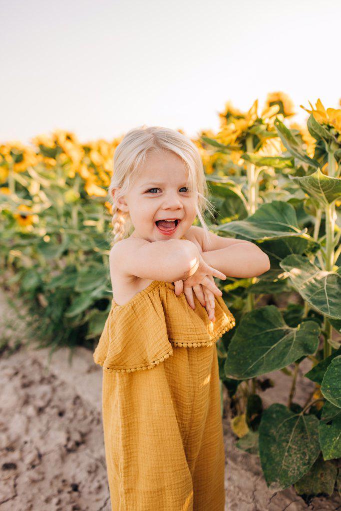 Two year old Caucasian girl laughs while playing in sunflowers
