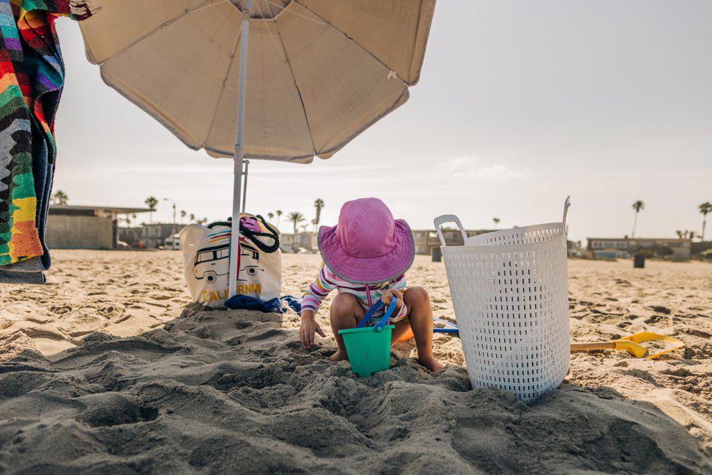 Toddler girl plays under umbrella in sand at Ocean Beach