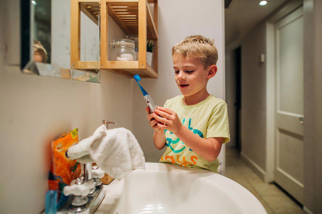 Young boy happily brushes teeth with electric toothbrush