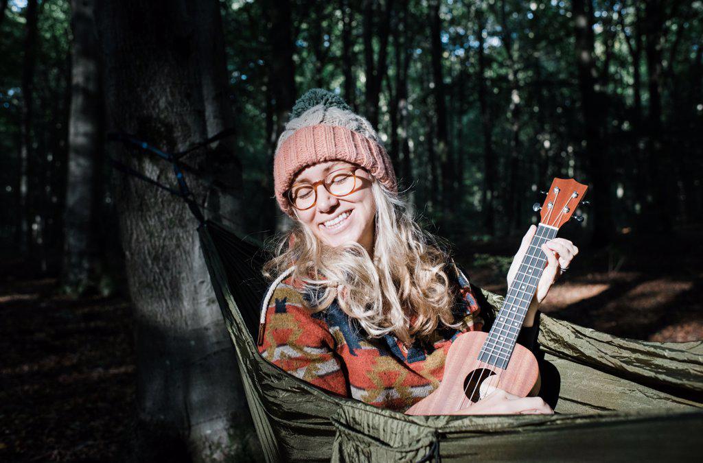 woman on a hammock playing ukulele in the forest