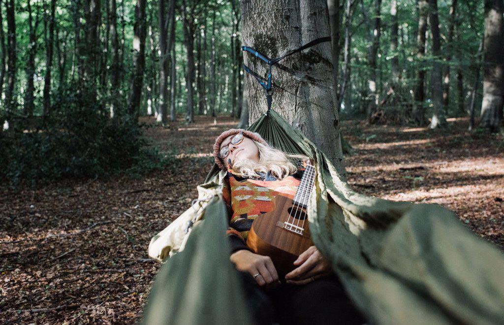 woman sleeping in a hammock with her ukulele in the forest