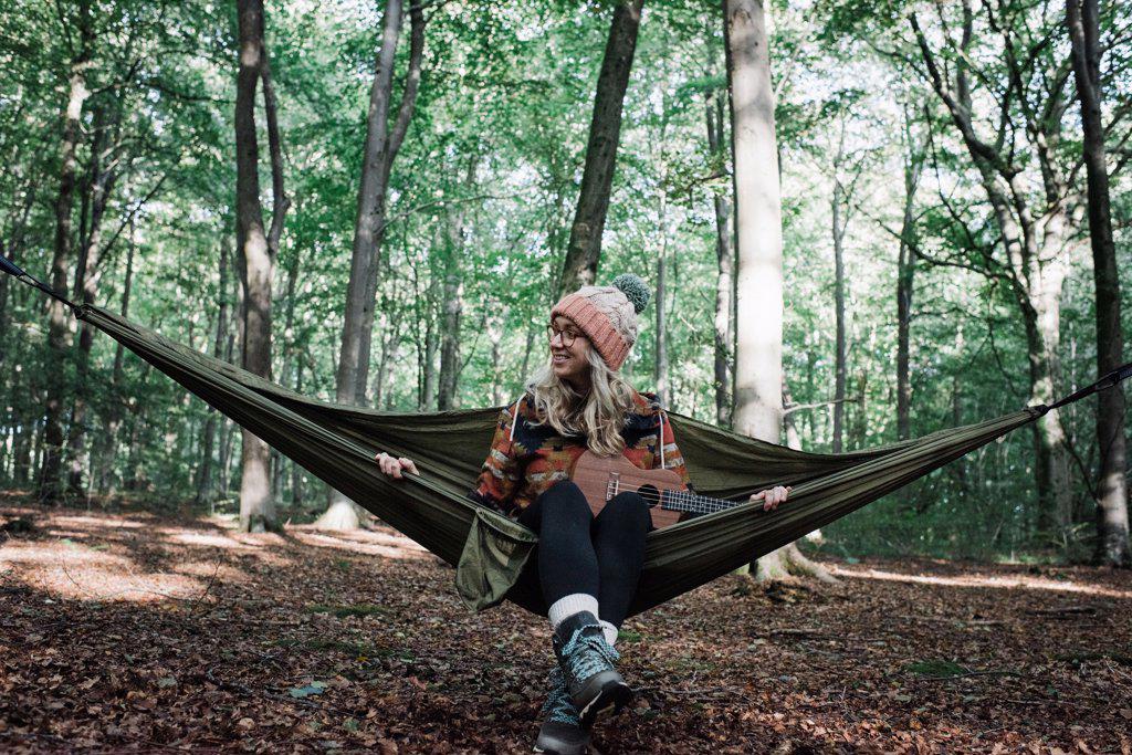 woman sat on a hammock in the forest with a ukulele in autumn