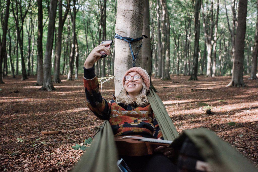 woman sat in a hammock in the forest taking a selfie