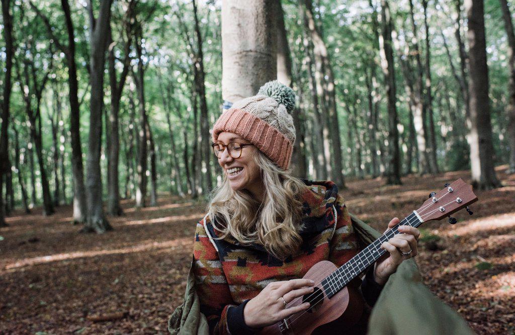 woman happily sat in a hammock playing the ukulele in a forest
