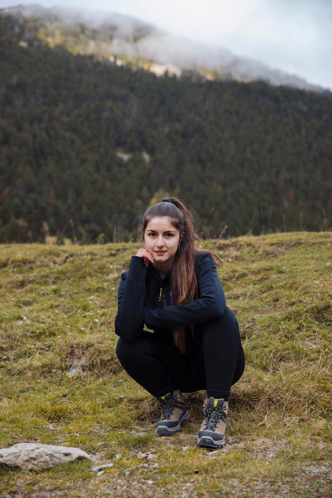 Brunette girl sitting while looking at camera in mountains