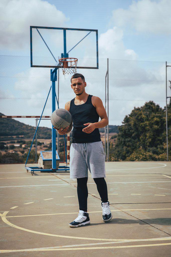 Young tattooed Latino boy playing with a basketball on a court