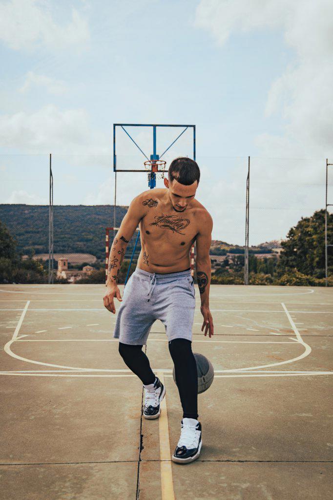 Young tattooed Latino boy playing with a basketball on a court