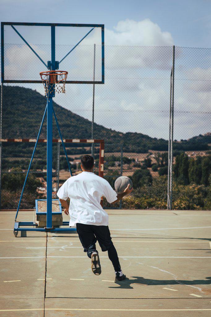 Young boy from his back playing with a basketball on a court