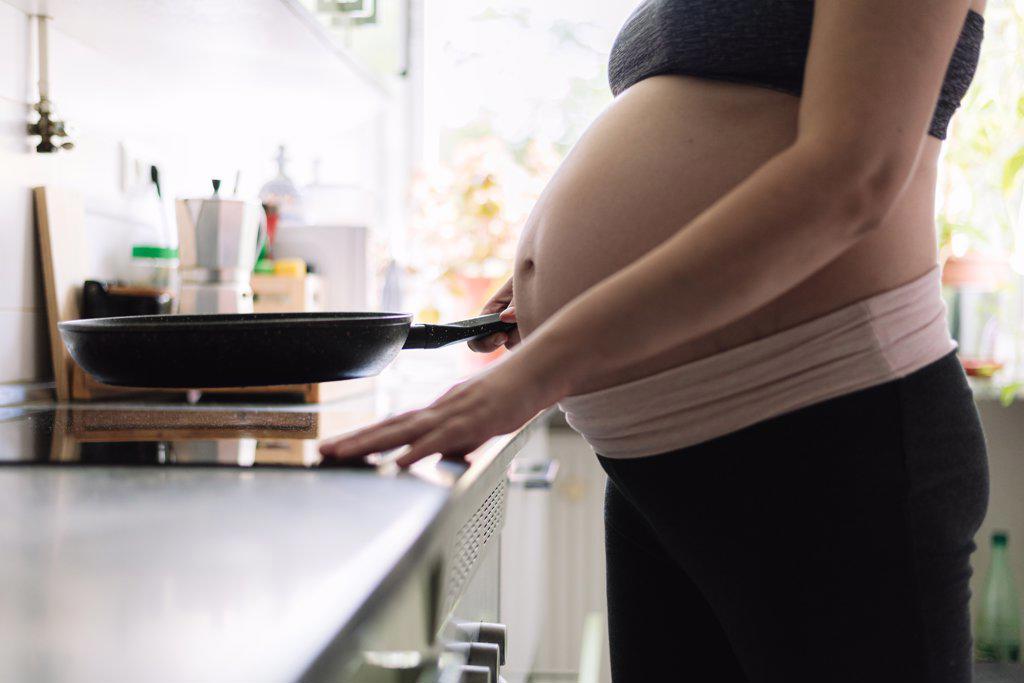 Pregnant woman cooking in the kitchen of her home.