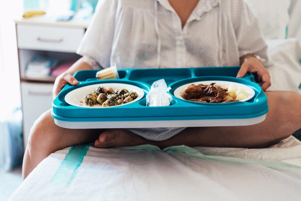 Young woman hospitalized in a bed. Holding hospital food tray.