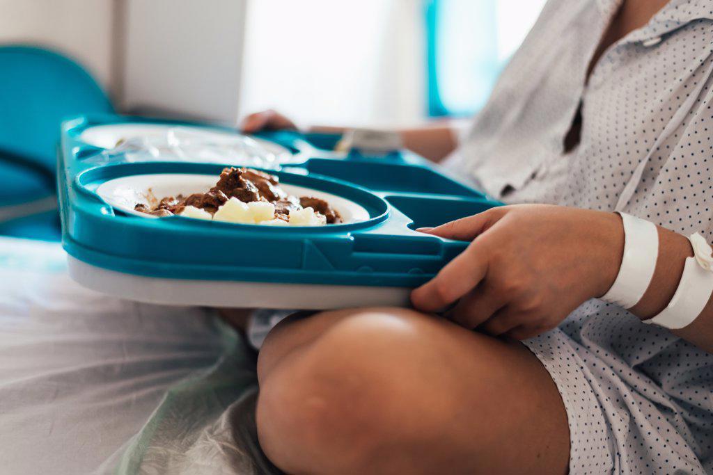 Young woman hospitalized in a bed. Holding hospital food tray.