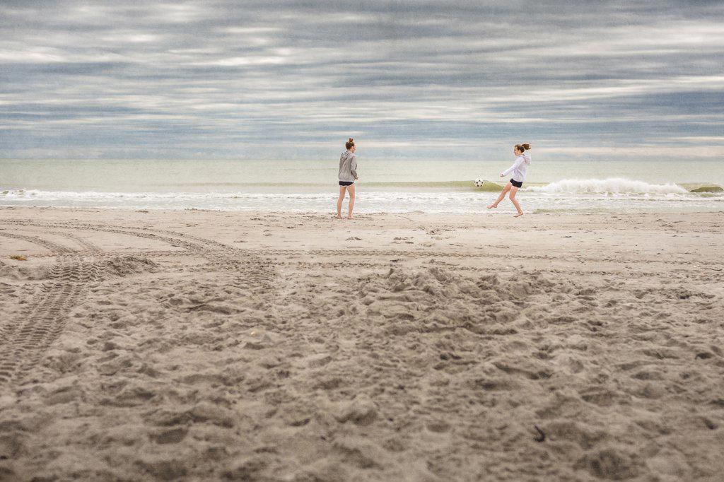Two girls in hoodies play soccer on a deserted Florida beach in winter