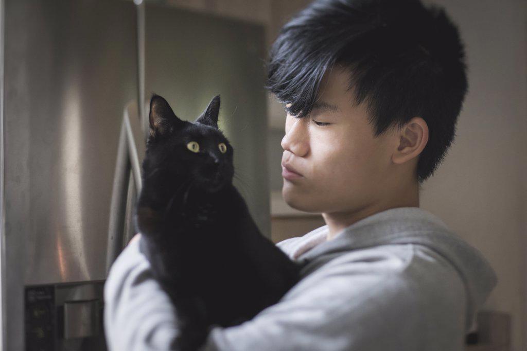 Asian teen boy in hoodie holds black cat