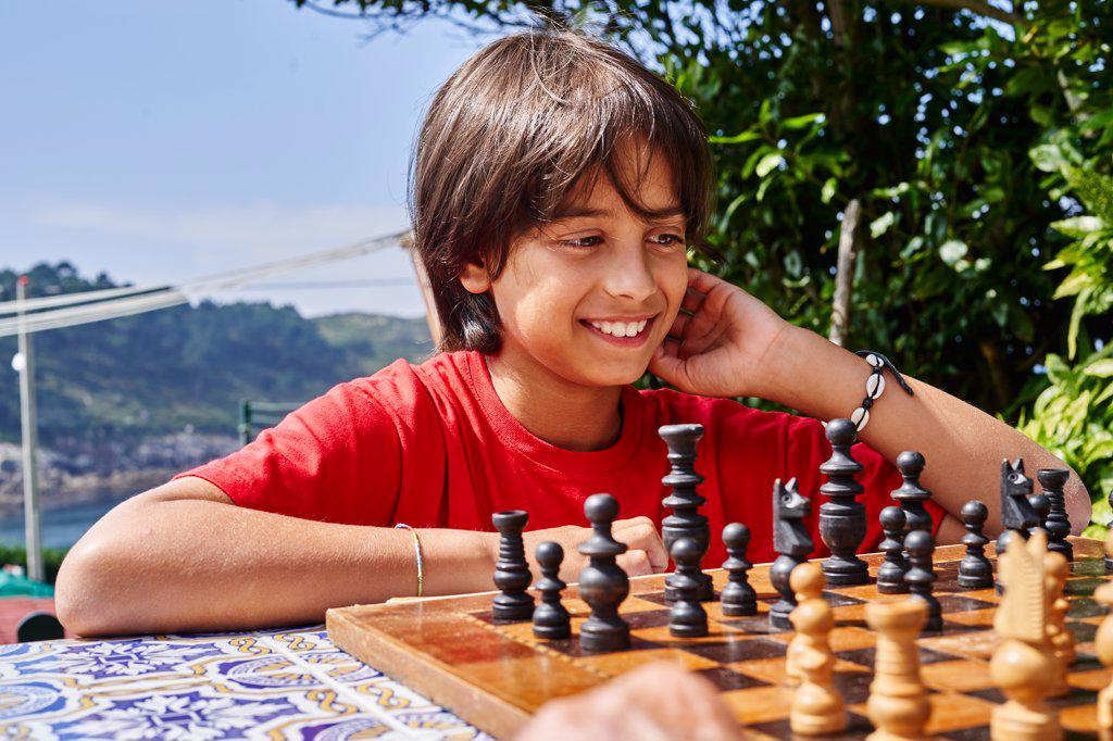 Young pensive boy sitting behind chess board moving one of the pieces.