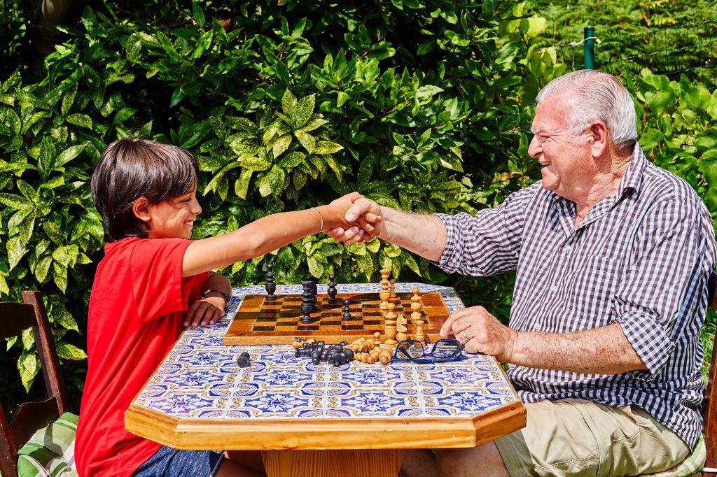Grandfather and grandson shaking hands over chessboard