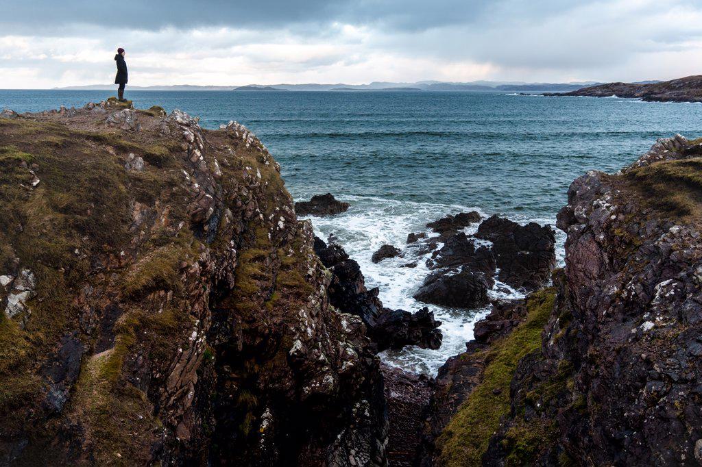 Solo woman standing on cliff above ocean