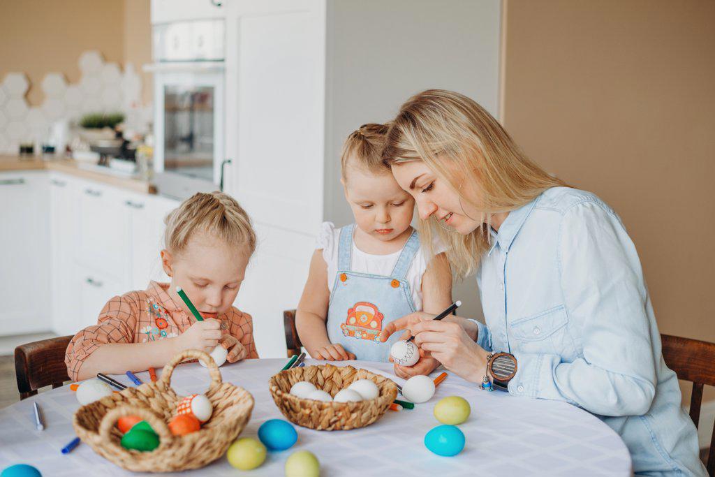 mom and daughters decorate eggs for easter