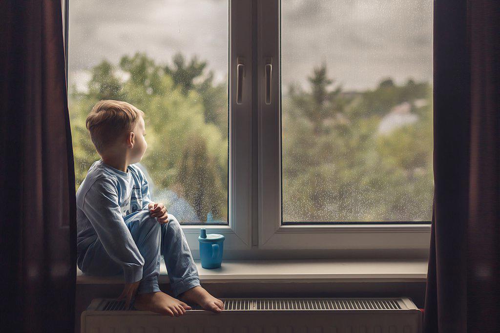 Side view of boy in blue pajamas sitting on windowsill