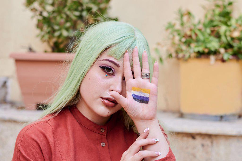 Person with green hair shows non-binary flag in the palm of her hand