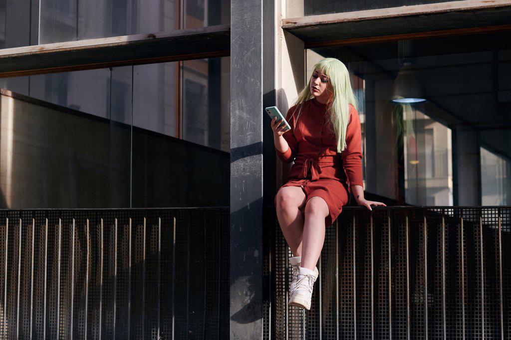 Young woman with green hair looks at her mobile on the street