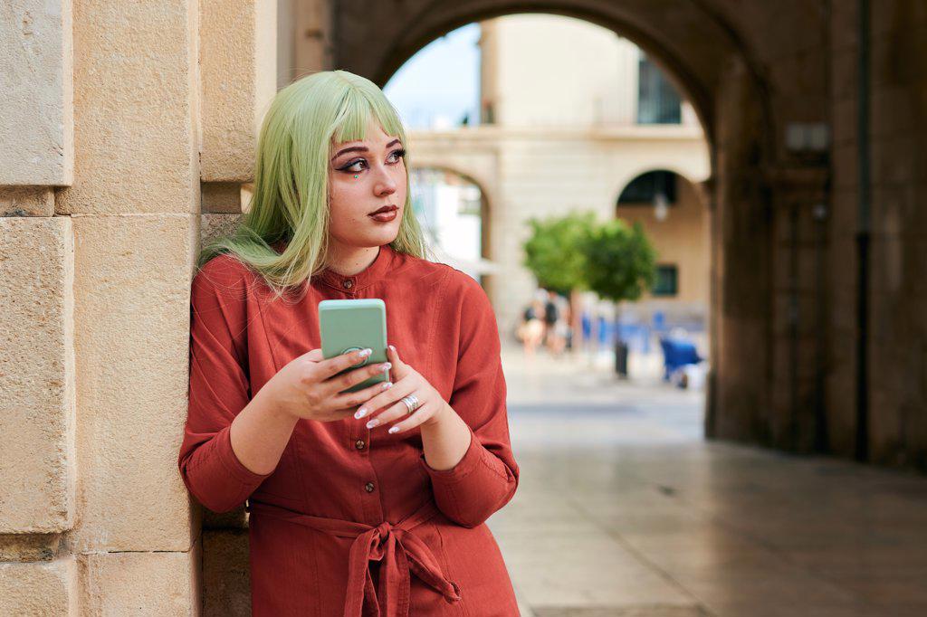 Non-binary person with a green wig holds a smartphone on the street